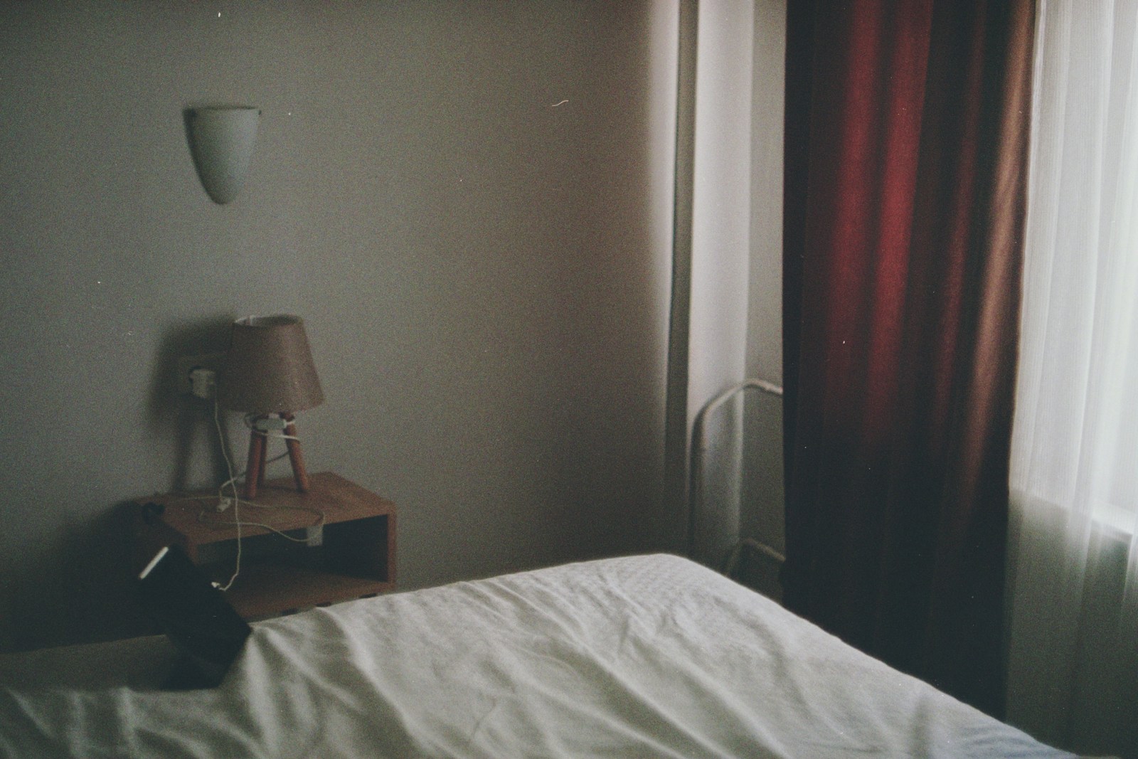 A simple hotel room with a bed, nightstand, and curtains